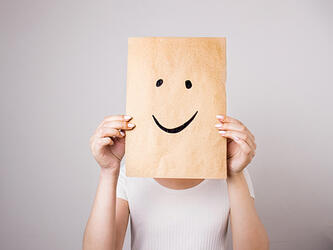 person holding piece of paper with similing face drawn on it